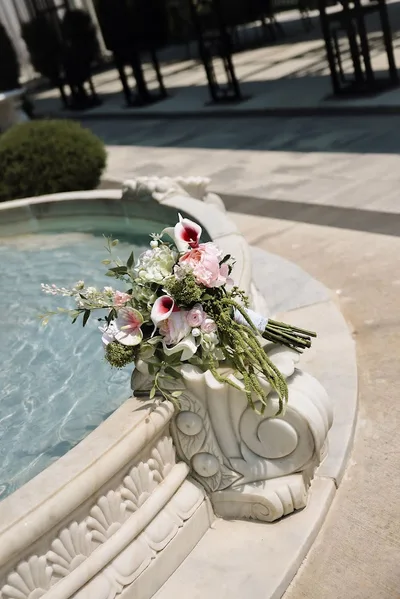 The bridal bouquet resting on the carved stone edge of a fountain.