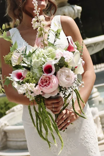 The bride holding a bouquet of calla lilies, garden roses and trailing amaranthus.