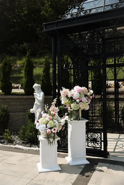 Two pedestal arrangements of blush and white florals set beside the garden pergola.