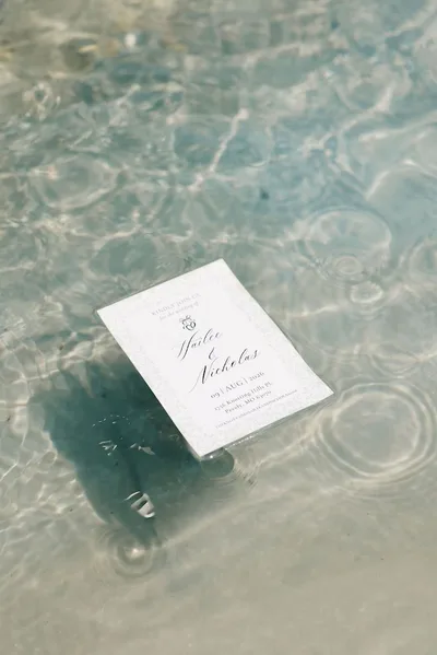 The wedding invitation floating in still, sunlit water.