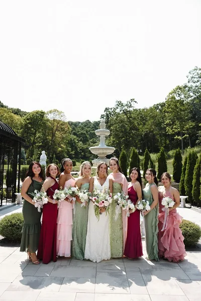 The bride and her attendants in mismatched green and pink gowns beside the fountain.