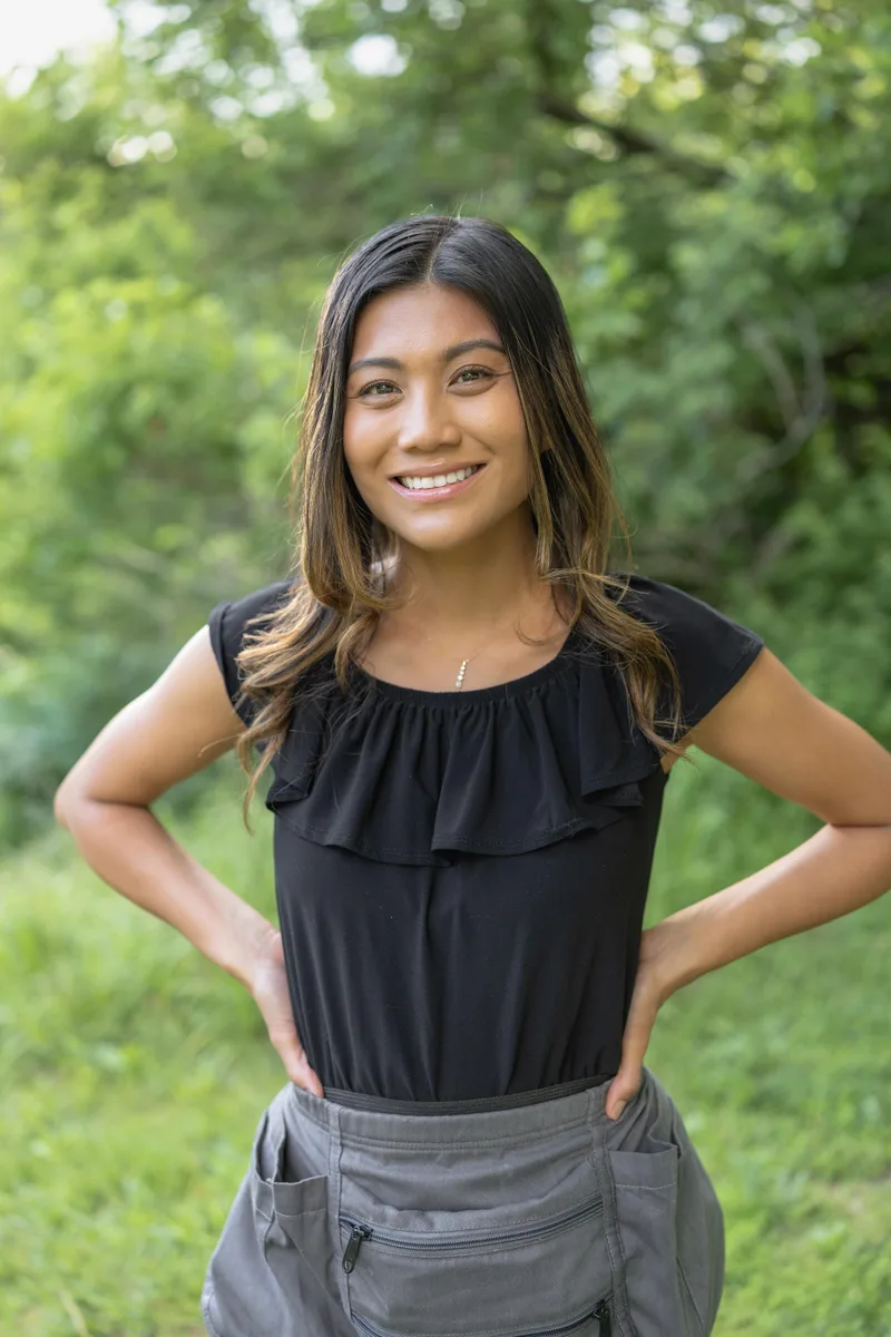 Klea Klingsick, owner and wedding coordinator behind Events By Klay, smiling outdoors in front of summer greenery.