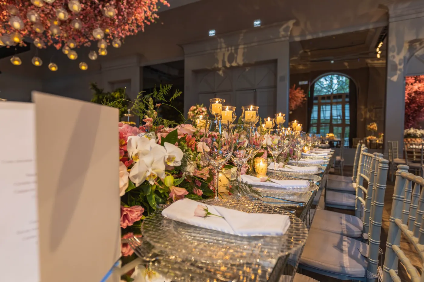 A candlelit reception head table dressed with blush and coral florals.