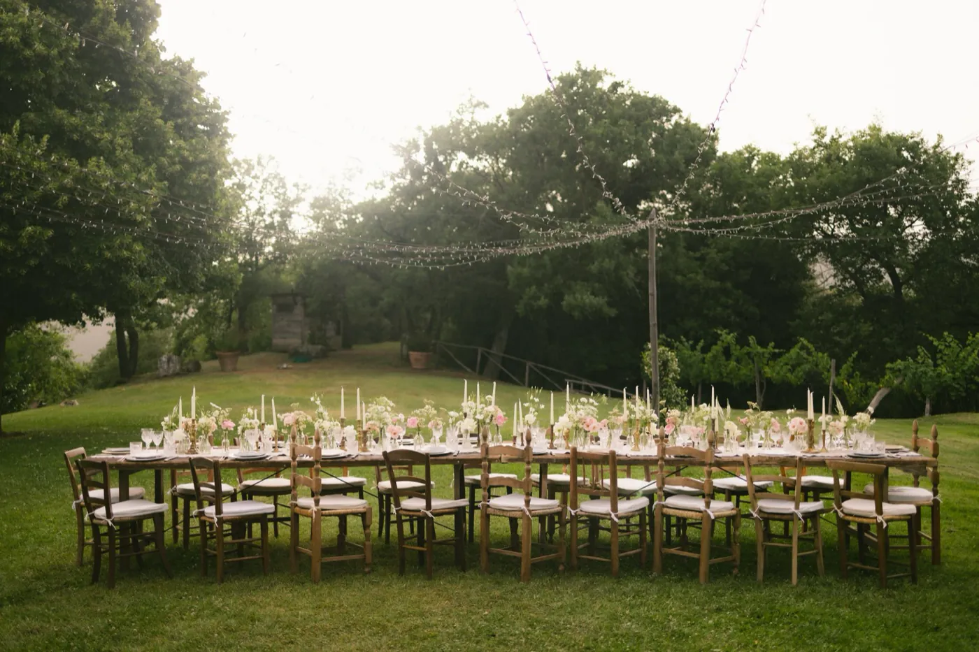 A long farm table set under fairy lights at golden dusk for an outdoor reception.