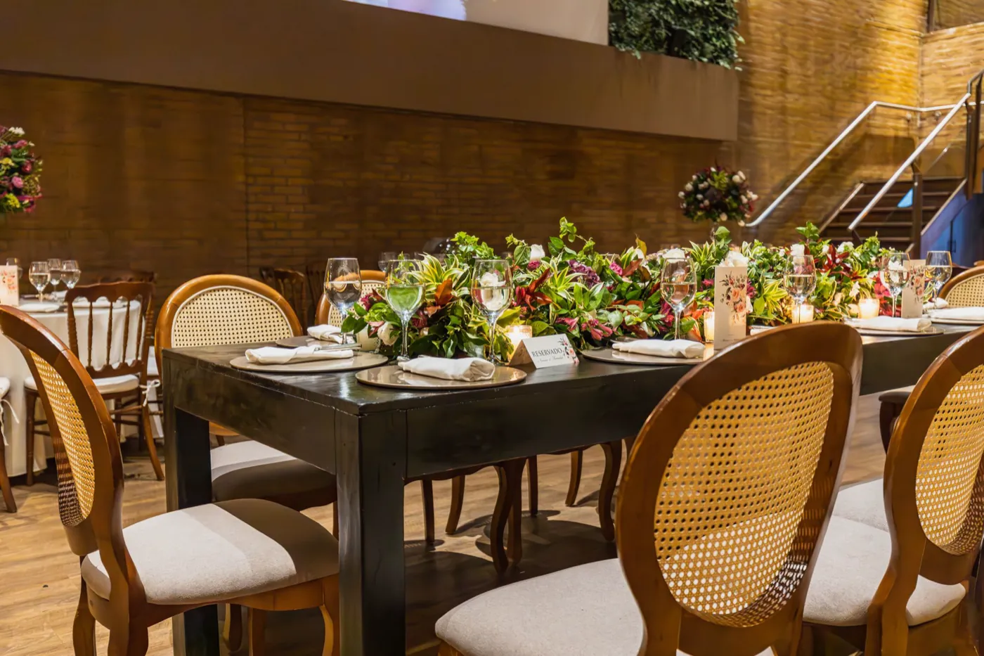 A warm wedding reception table with cane-back chairs and a lush greenery runner.